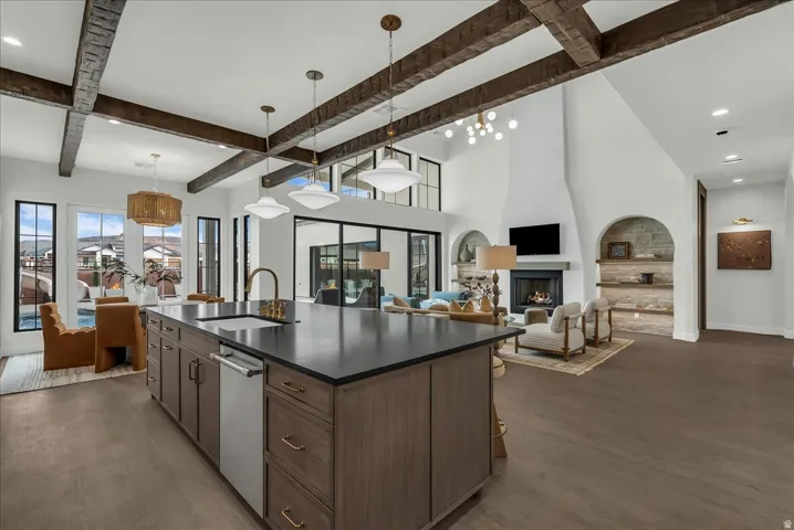 Kitchen with open floor plan, beamed ceiling, a fireplace, a center island with sink, and hanging light fixtures