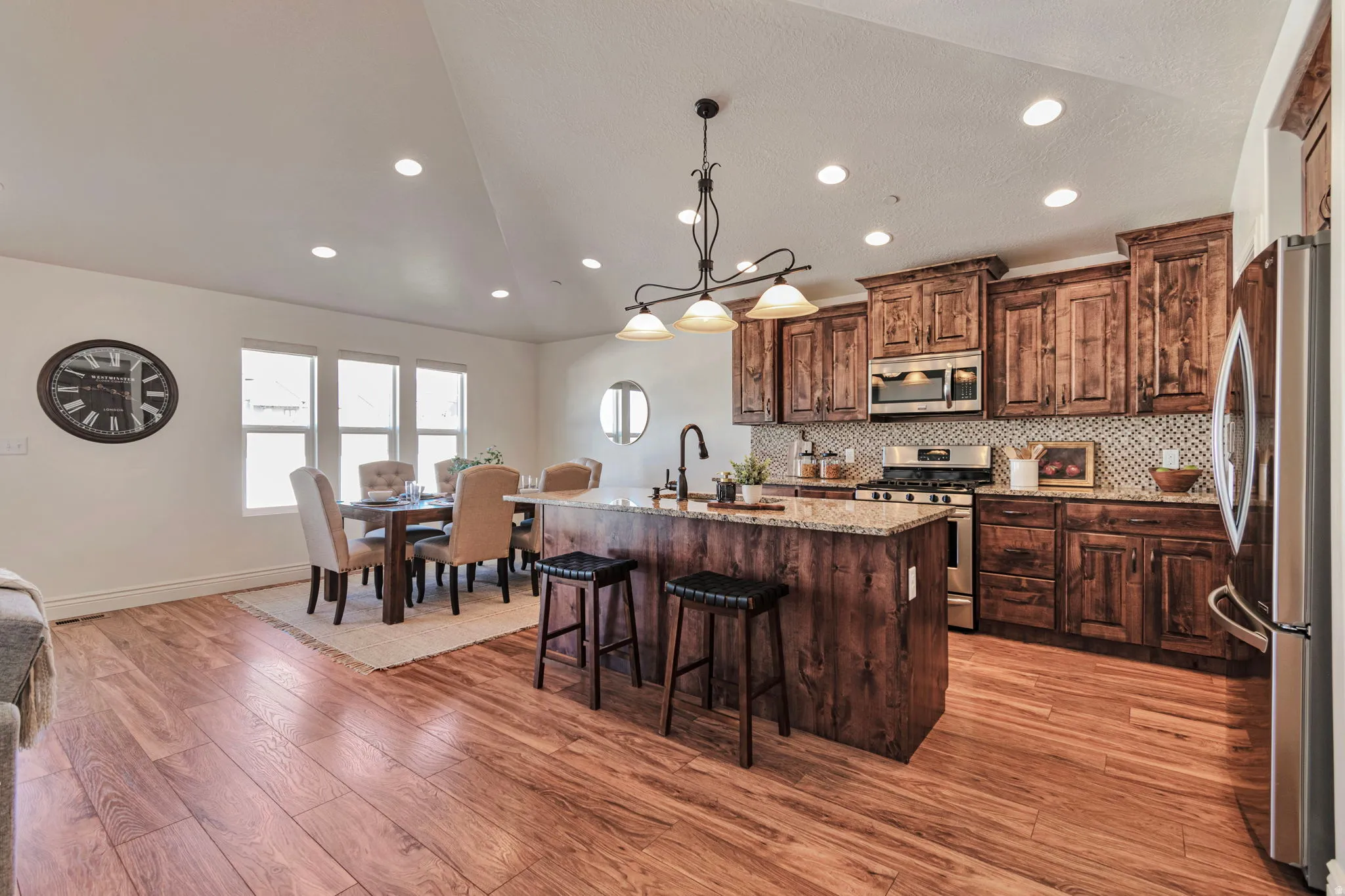 Kitchen with stainless steel appliances, light stone counters, an island with sink, pendant lighting, and light wood-style floors