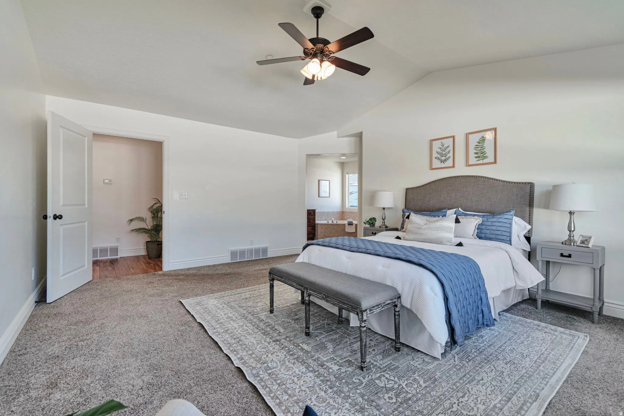 Carpeted bedroom featuring ceiling fan, lofted ceiling, and ensuite bathroom