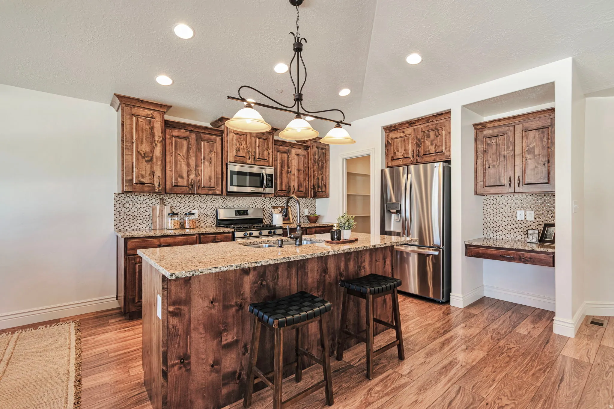 Kitchen featuring tasteful backsplash, light wood-type flooring, stainless steel appliances, light stone countertops, and wood finish cabinets