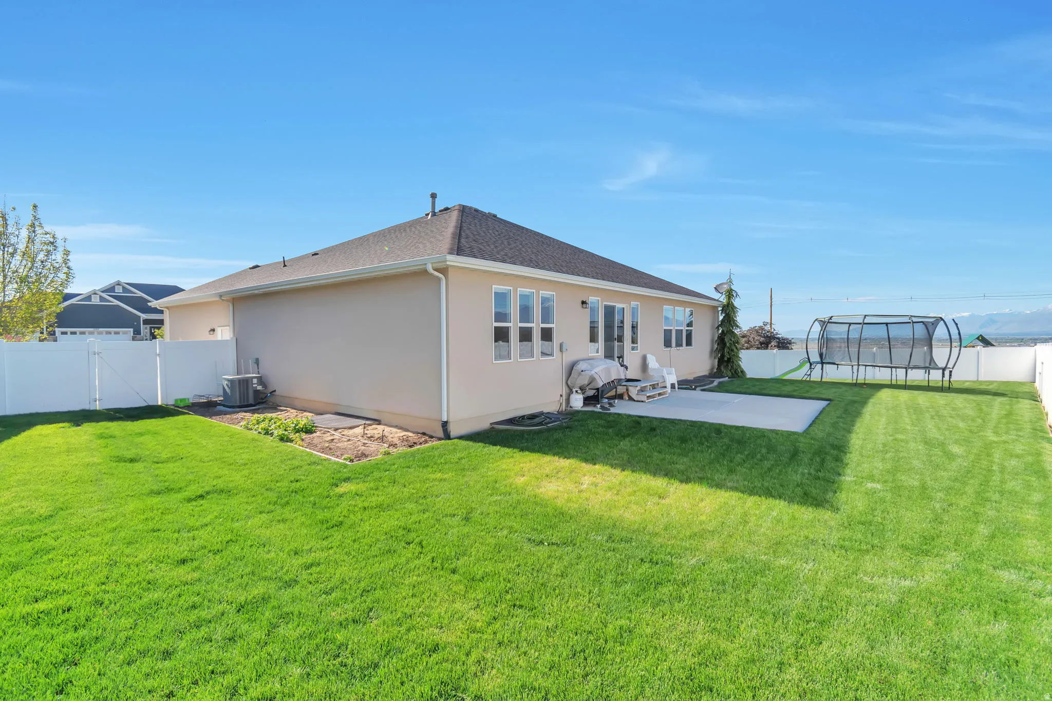 Rear view of property with a fenced backyard, a trampoline, a patio area, stucco siding, and a gate