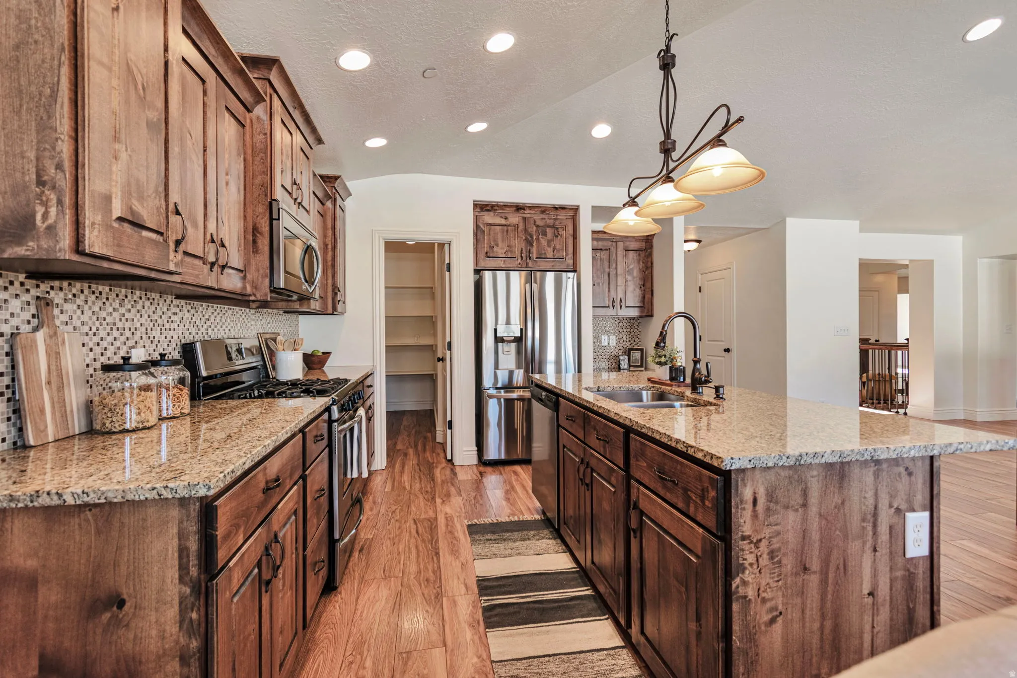 Kitchen featuring stainless steel appliances, light stone counters, light wood finished floors, an island with sink, and backsplash