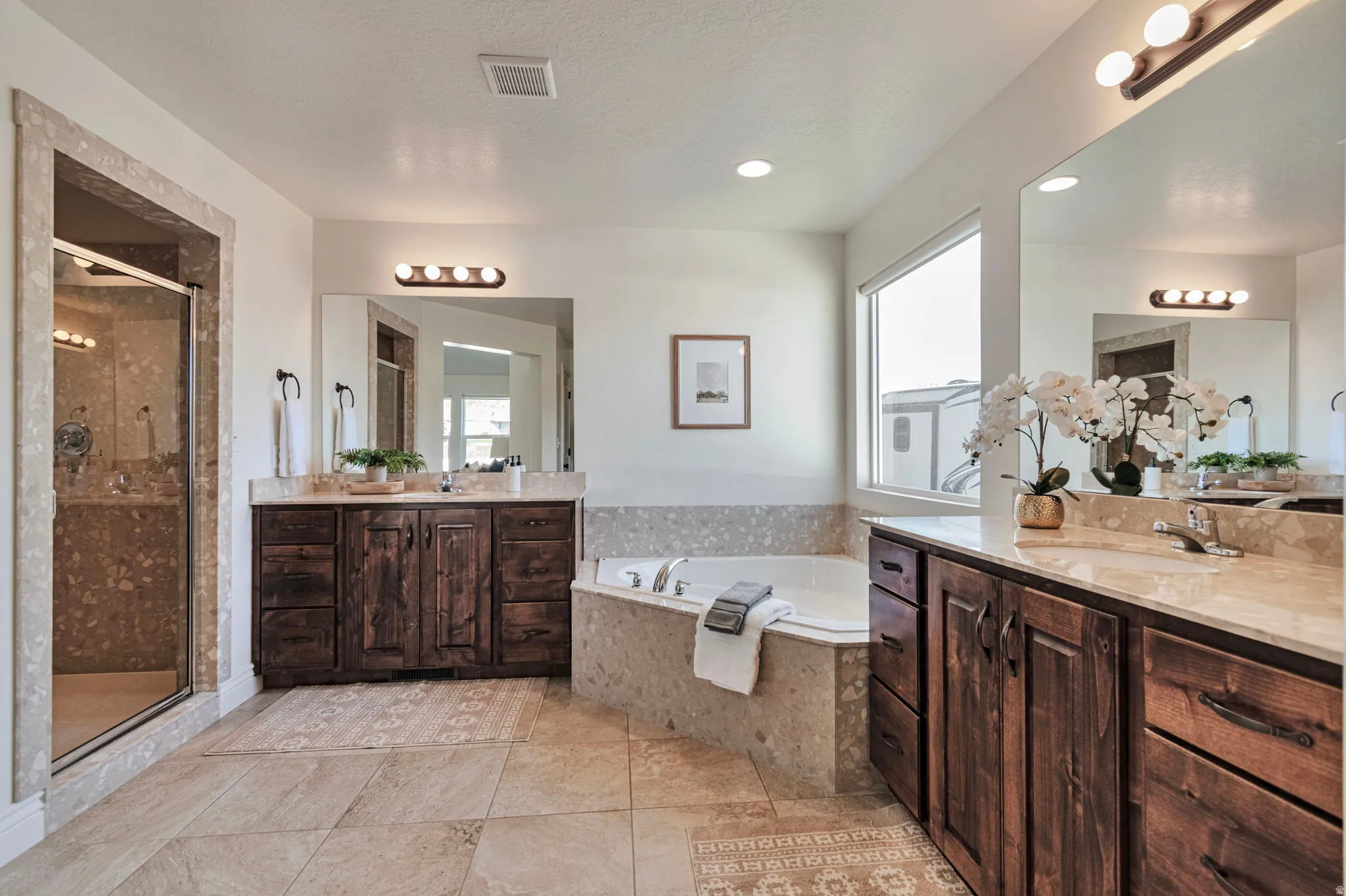 Bathroom featuring two vanities, a shower stall, and a garden tub