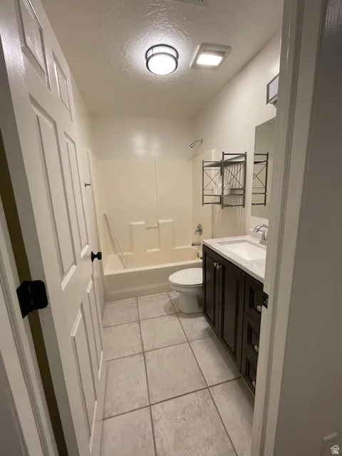 Full bath with a textured ceiling, vanity, tub / shower combination, and light tile patterned floors