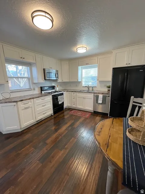Kitchen with appliances with stainless steel finishes, white cabinets, a textured ceiling, and dark wood-style floors