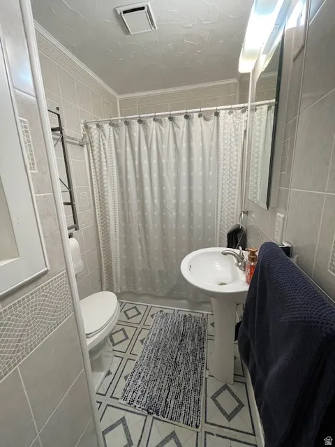 Bathroom with tile walls, a shower with shower curtain, crown molding, a textured ceiling, and light tile patterned floors