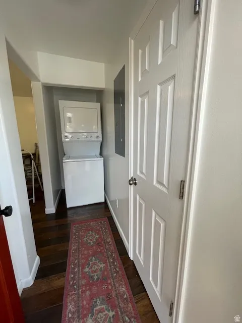 Laundry area featuring stacked washing machine and dryer, dark wood-type flooring, and electric panel