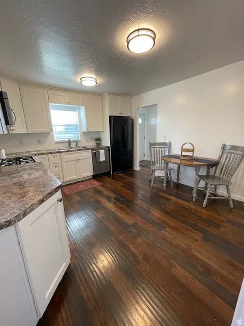 Kitchen with dark countertops, dark wood-type flooring, a textured ceiling, freestanding refrigerator, and white cabinets