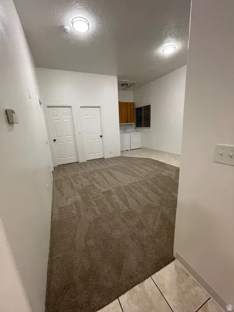 Unfurnished living room with a textured ceiling, light colored carpet, light tile patterned floors, and washer and clothes dryer