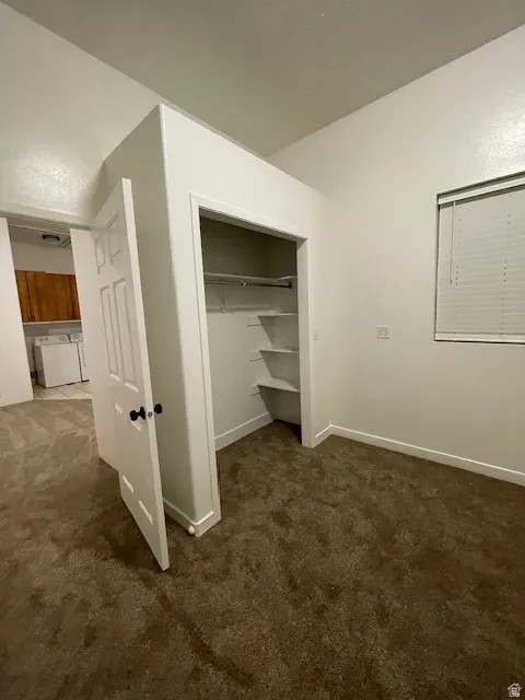 Unfurnished bedroom featuring dark colored carpet, a closet, and washer and dryer