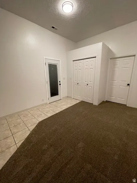 Unfurnished bedroom featuring a textured ceiling, light tile patterned floors, light carpet, and a closet