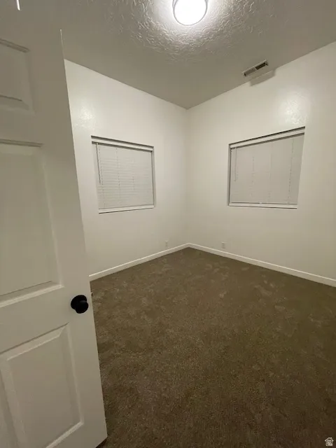 Unfurnished room with dark colored carpet and a textured ceiling
