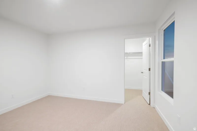 Unfurnished bedroom with a walk in closet and light carpet