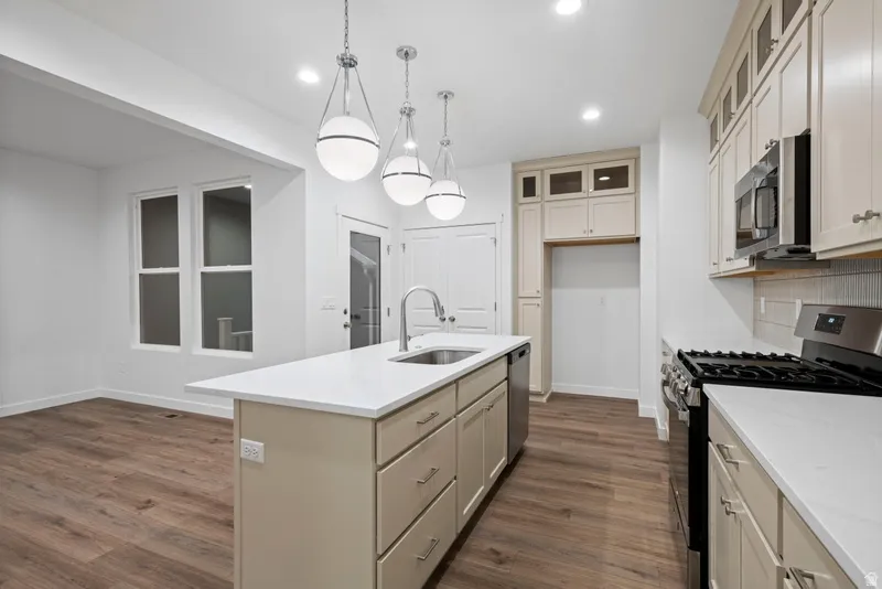 Kitchen featuring stainless steel appliances, cream cabinets, glass insert cabinets, dark wood-type flooring, and recessed lighting