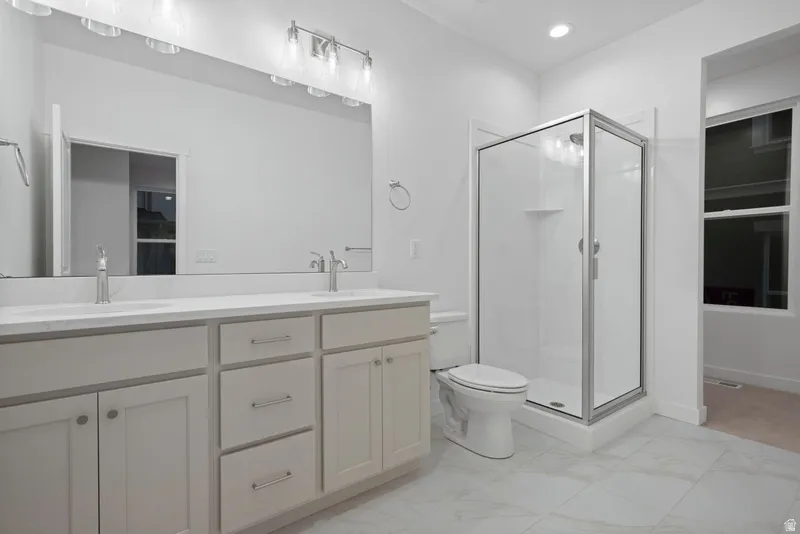 Full bathroom featuring double vanity, a stall shower, light marble finish floors, and recessed lighting