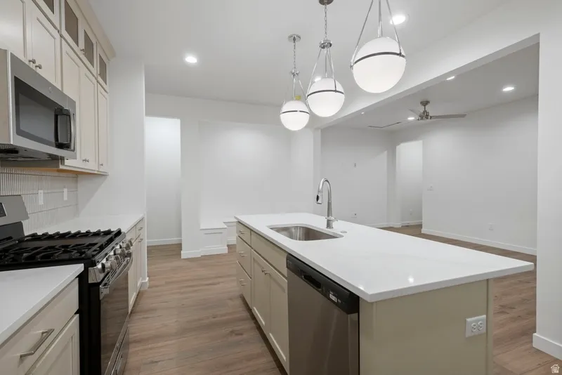 Kitchen with appliances with stainless steel finishes, dark wood finished floors, recessed lighting, ceiling fan, and a kitchen island with sink
