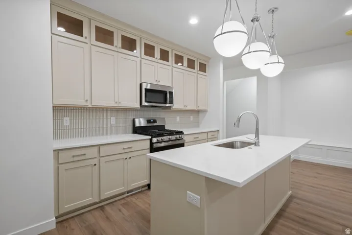 Kitchen featuring cream cabinetry, backsplash, appliances with stainless steel finishes, glass insert cabinets, and a kitchen island with sink
