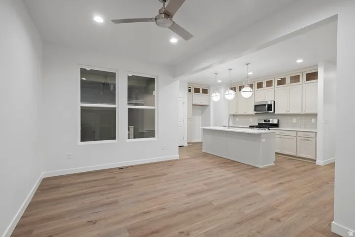 Kitchen featuring recessed lighting, light countertops, light wood-type flooring, a center island with sink, and decorative light fixtures