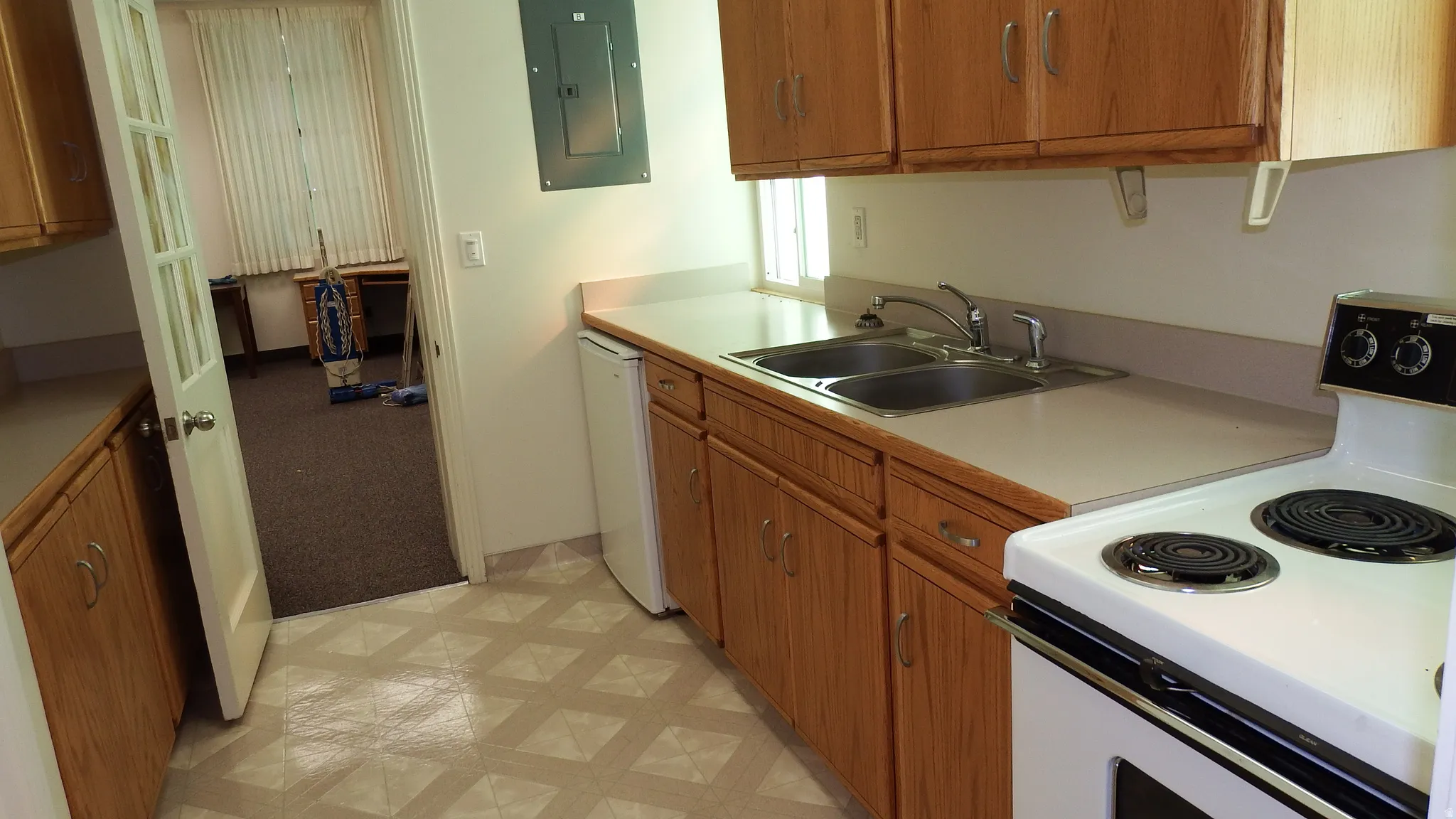 Kitchen featuring white appliances, brown cabinets, light countertops, electric panel, and light flooring