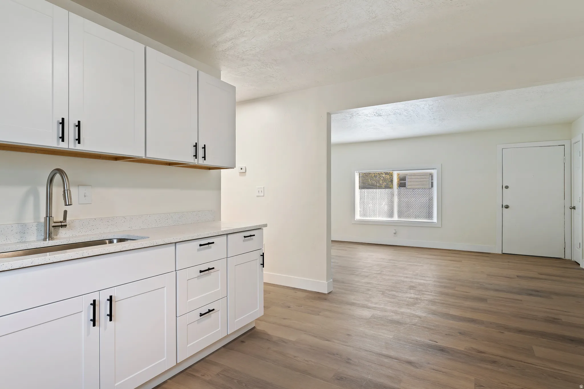 Unit 2 Kitchen with a textured ceiling, white cabinets, light stone countertops, and light wood finished floors