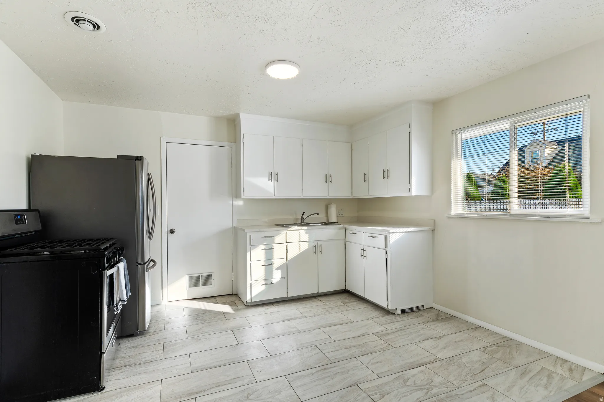 Unit 1 Kitchen with stainless steel fridge and gas stove, light countertops, white cabinets, and a textured ceiling