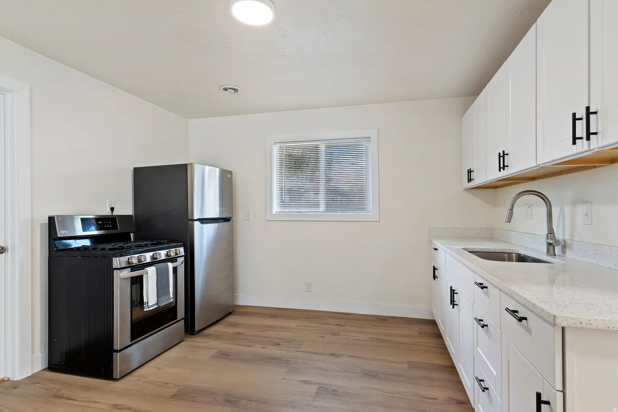 Unit 2 Kitchen with stainless steel fridge and gas stove, light countertops, white cabinets