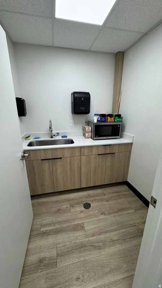 Kitchen featuring light countertops, light wood-style flooring, a drop ceiling, stainless steel microwave, and brown cabinetry