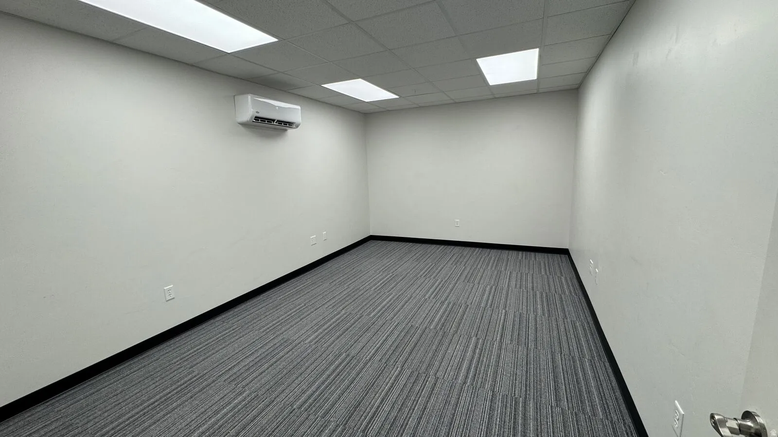 Carpeted spare room featuring a paneled ceiling and a wall mounted air conditioner
