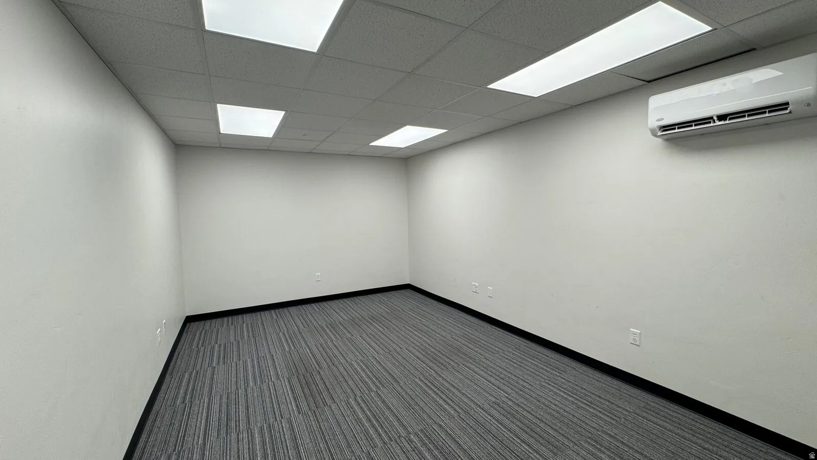 Unfurnished room with a wall mounted air conditioner, dark carpet, and a paneled ceiling
