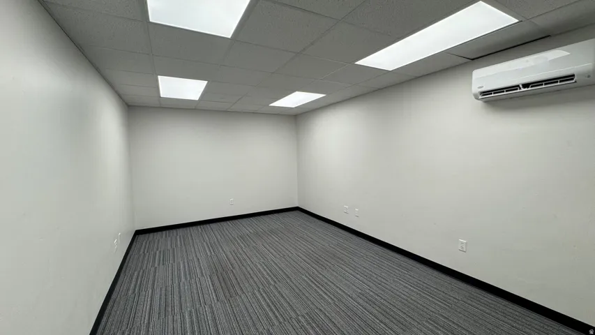 Unfurnished room with a wall mounted air conditioner, dark carpet, and a paneled ceiling