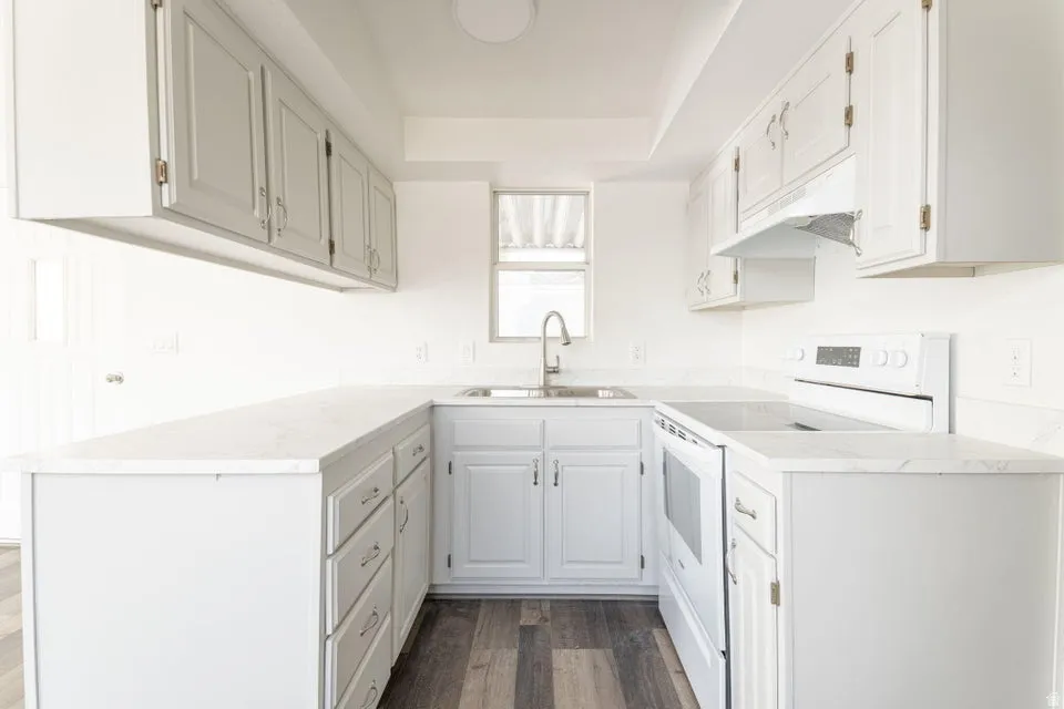 Kitchen with white electric range oven, dark wood-type flooring, under cabinet range hood, and white cabinets