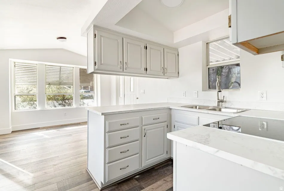 Kitchen featuring light countertops, light wood-style flooring, a peninsula, vaulted ceiling, and electric cooktop