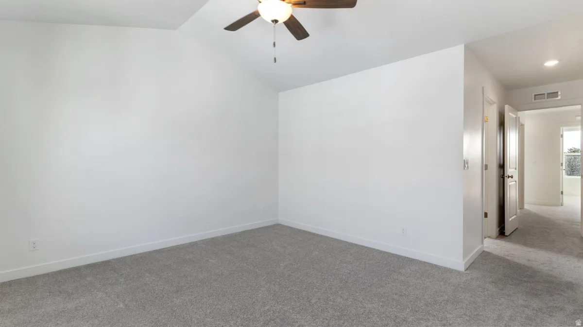 Empty room with carpet flooring, a ceiling fan, and vaulted ceiling