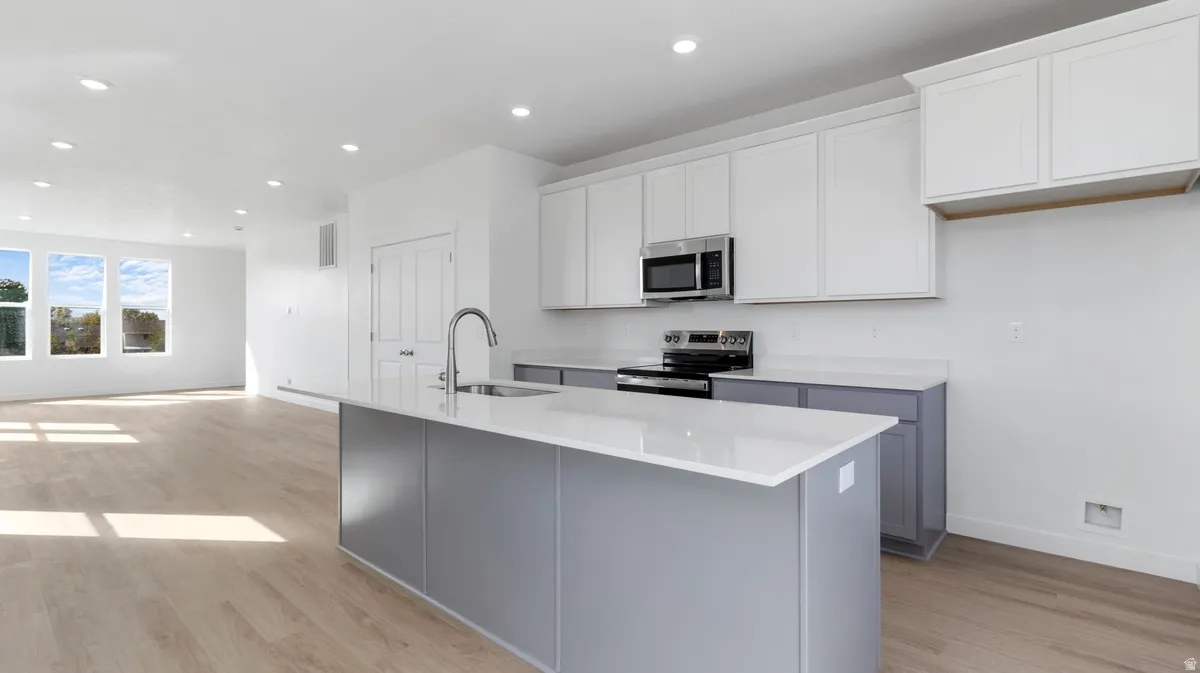 Kitchen with white cabinets, light wood-style flooring, stainless steel appliances, recessed lighting, and a center island with sink