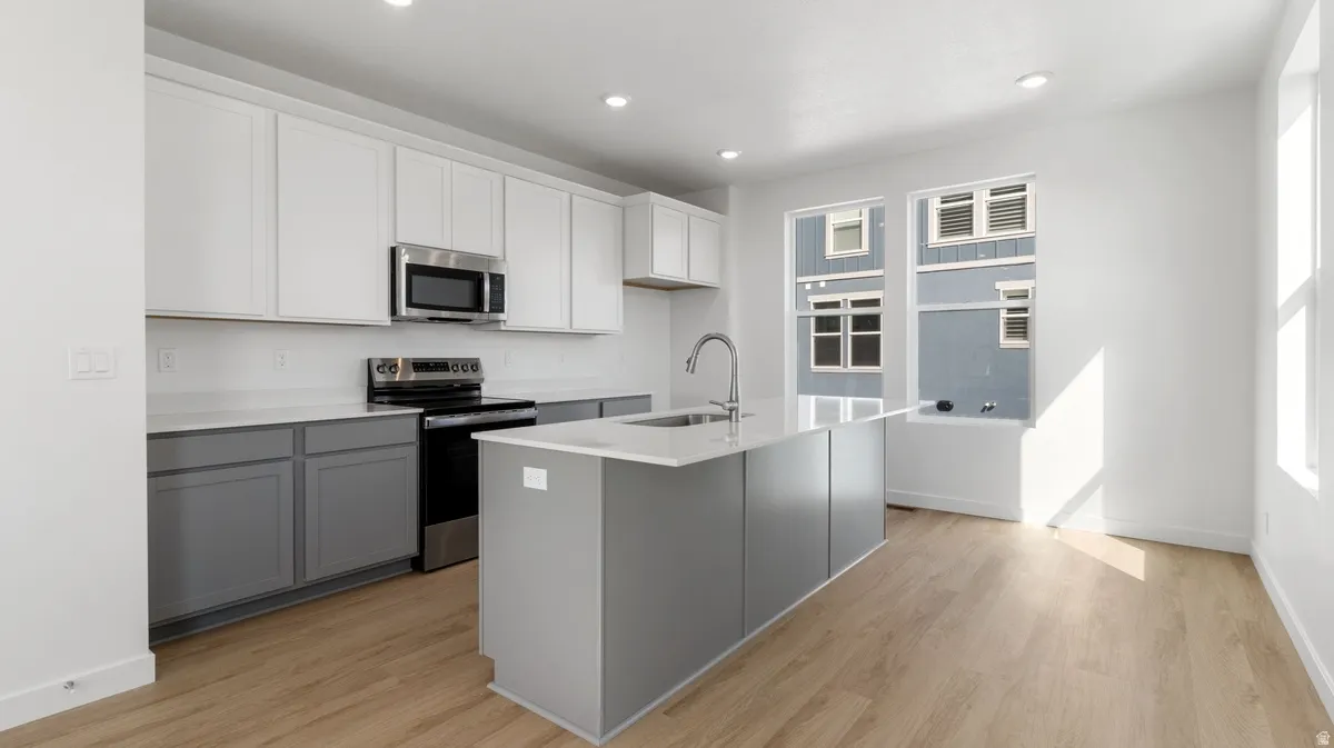 Kitchen featuring appliances with stainless steel finishes, gray cabinets, light wood finished floors, a kitchen island with sink, and recessed lighting