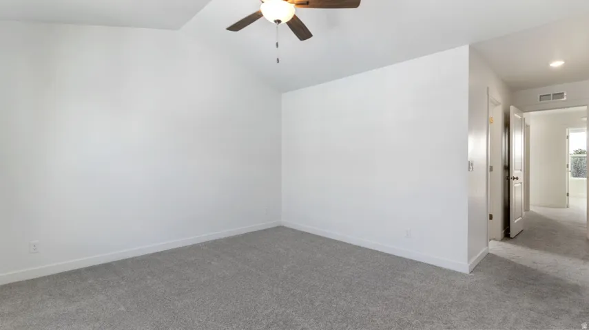 Empty room with carpet flooring, a ceiling fan, and vaulted ceiling