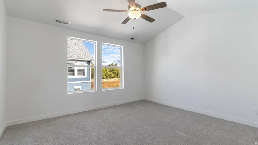 Unfurnished room with light colored carpet, vaulted ceiling, and ceiling fan