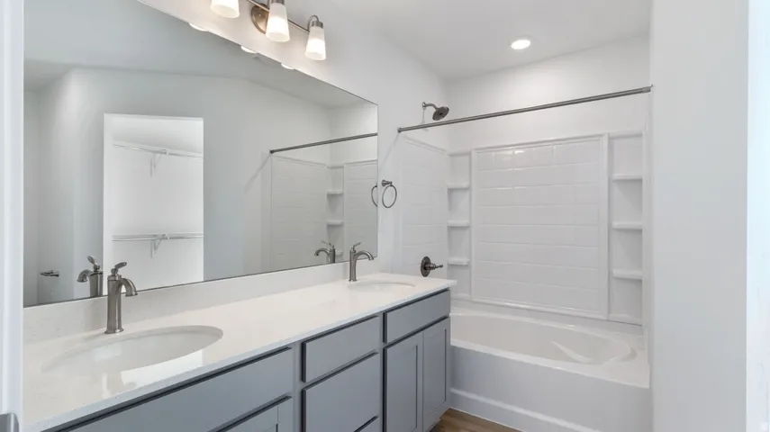 Full bath with a spacious closet, double vanity, tub / shower combination, and recessed lighting