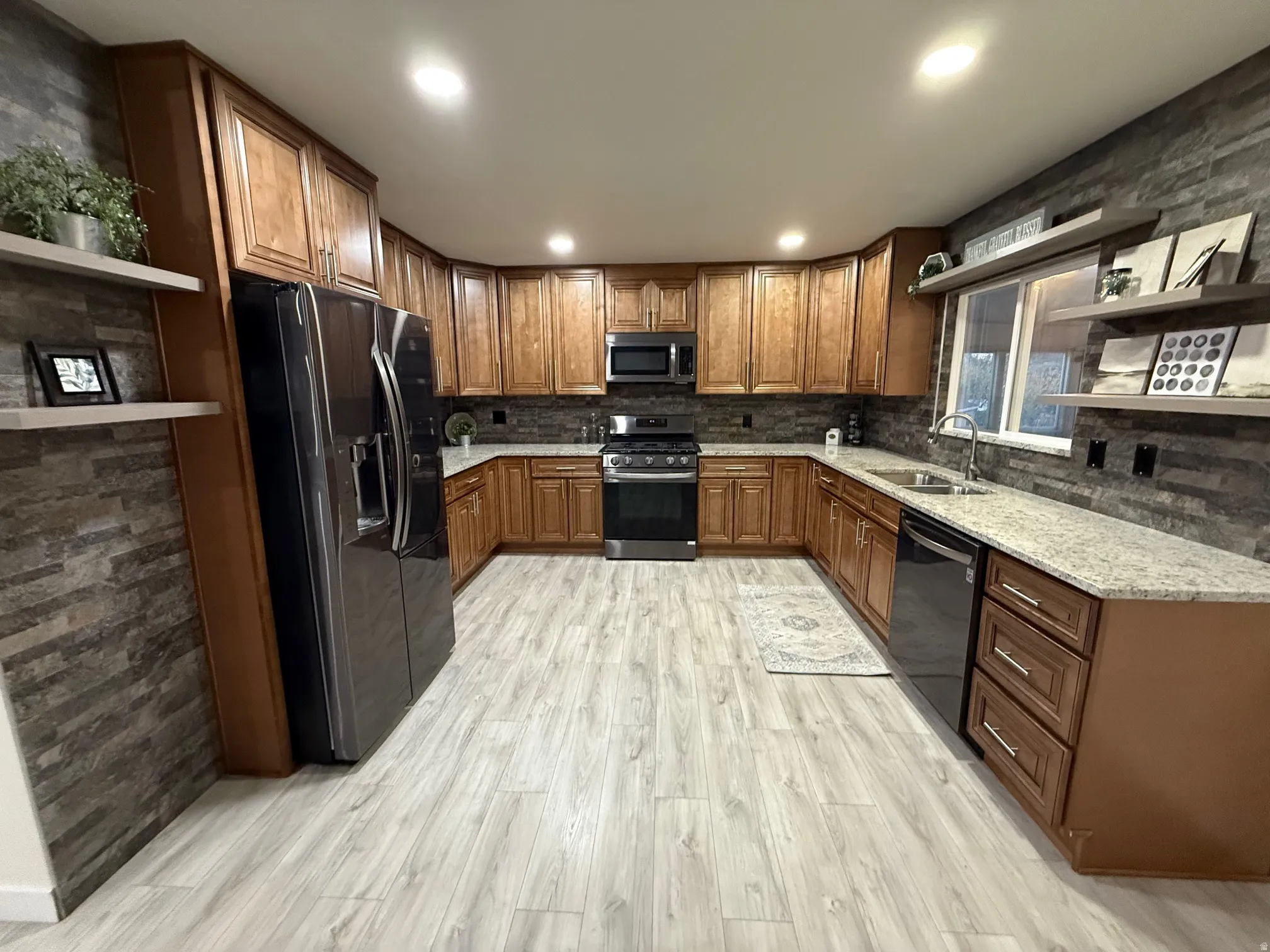 Kitchen with open shelves, light stone countertops, black appliances, brown cabinetry, and light wood finished floors