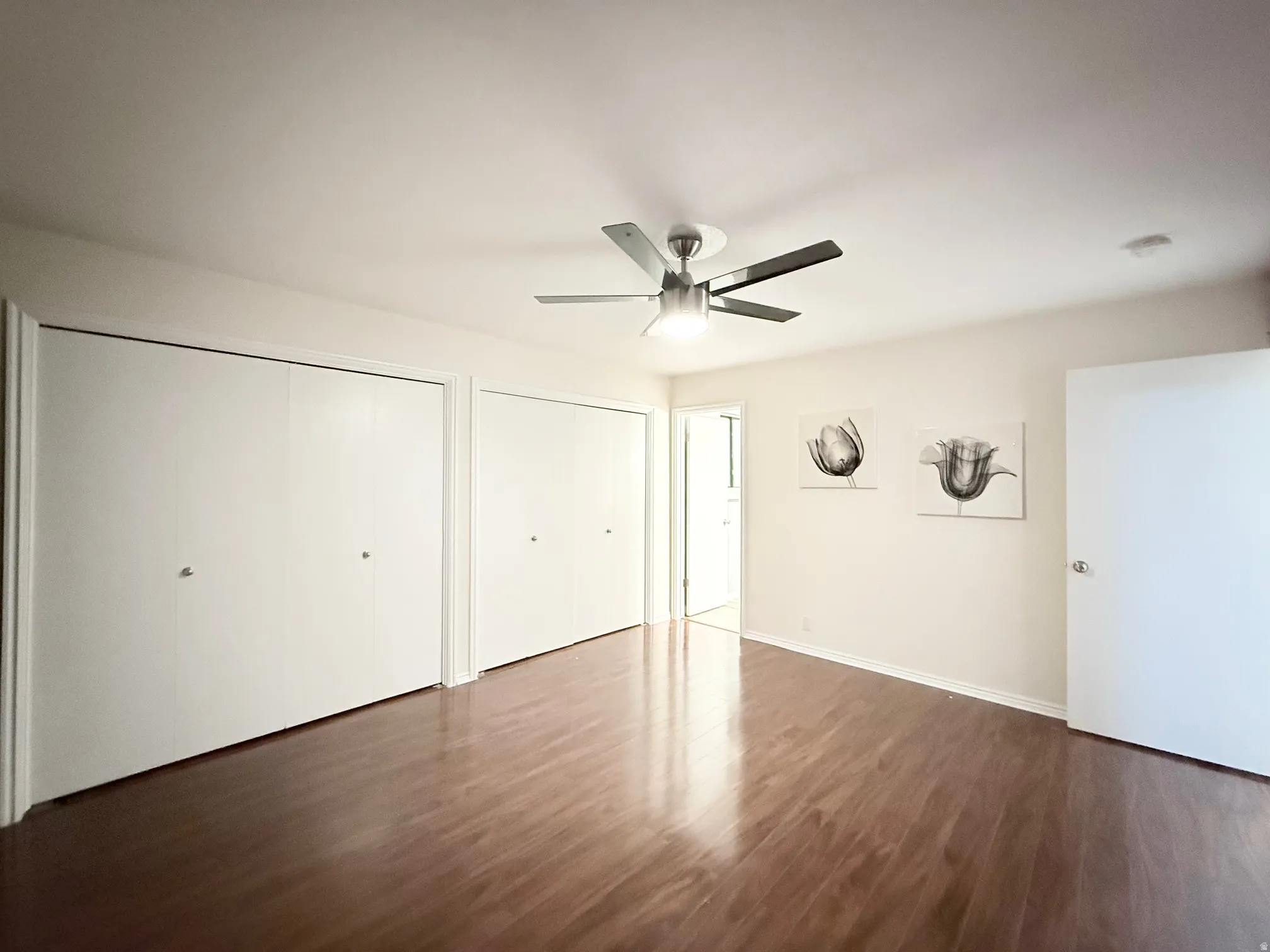 Unfurnished bedroom featuring two closets, dark wood finished floors, and a ceiling fan