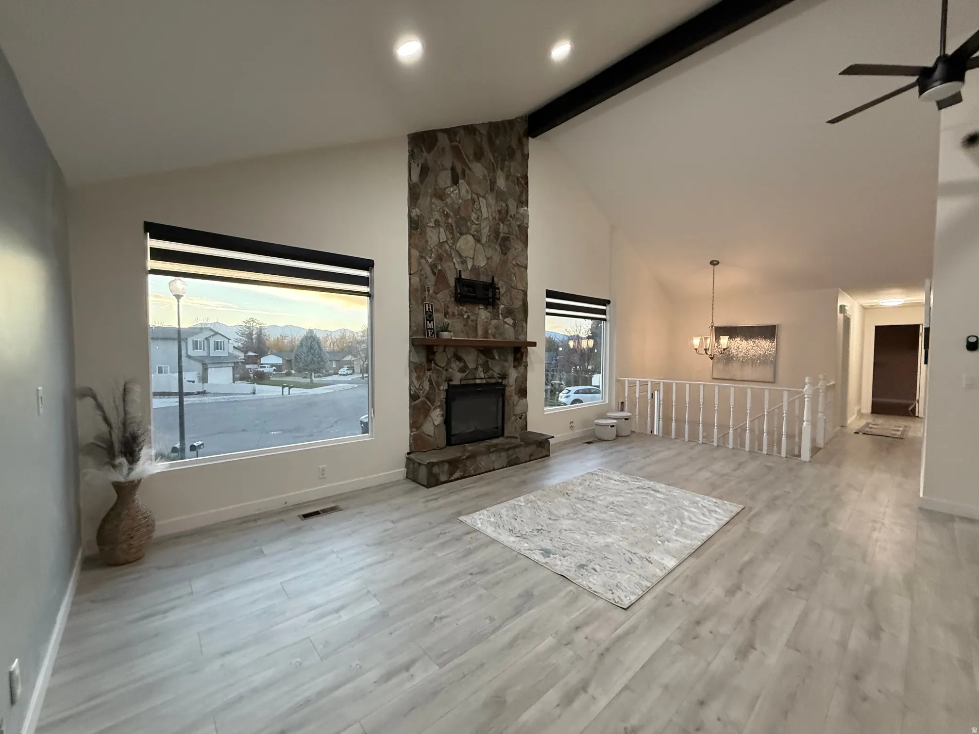 Unfurnished living room featuring beamed ceiling, a chandelier, light wood-type flooring, a stone fireplace, and high vaulted ceiling