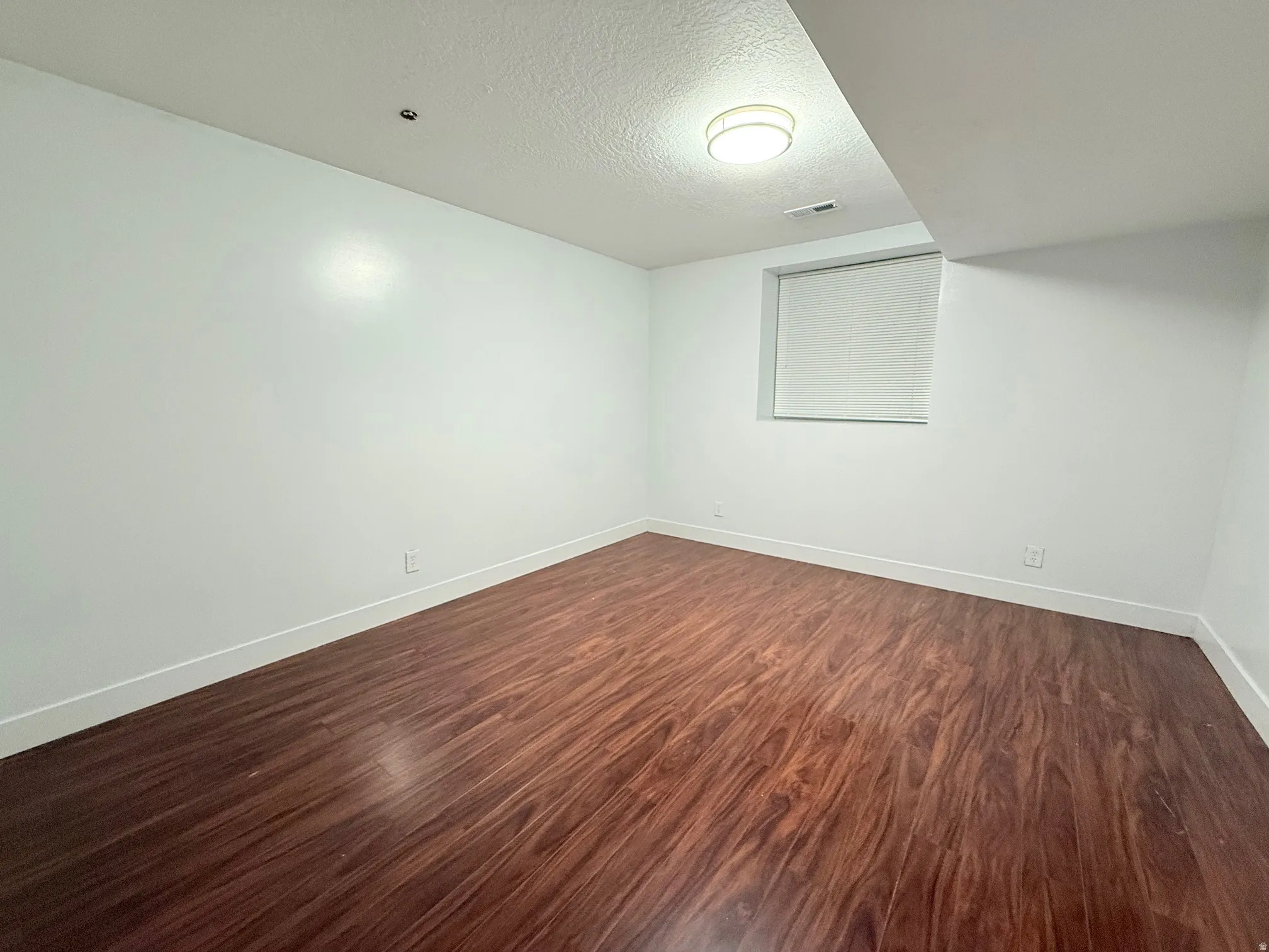 Empty room with a textured ceiling and dark wood-type flooring