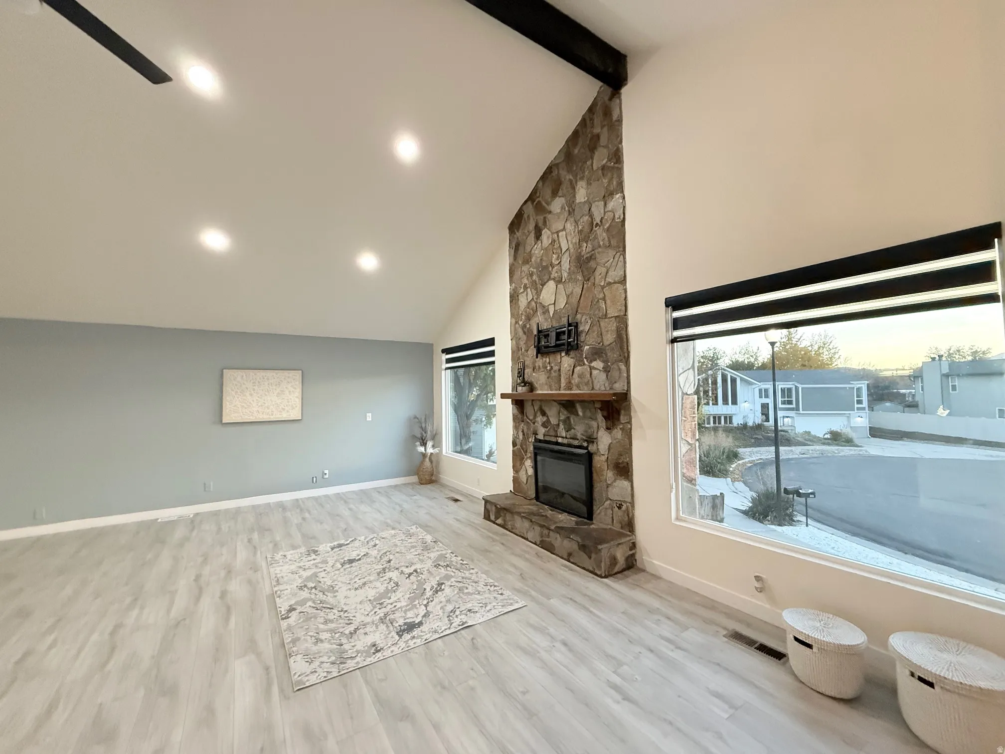 Living area with high vaulted ceiling, beam ceiling, plenty of natural light, light wood-style flooring, and a fireplace
