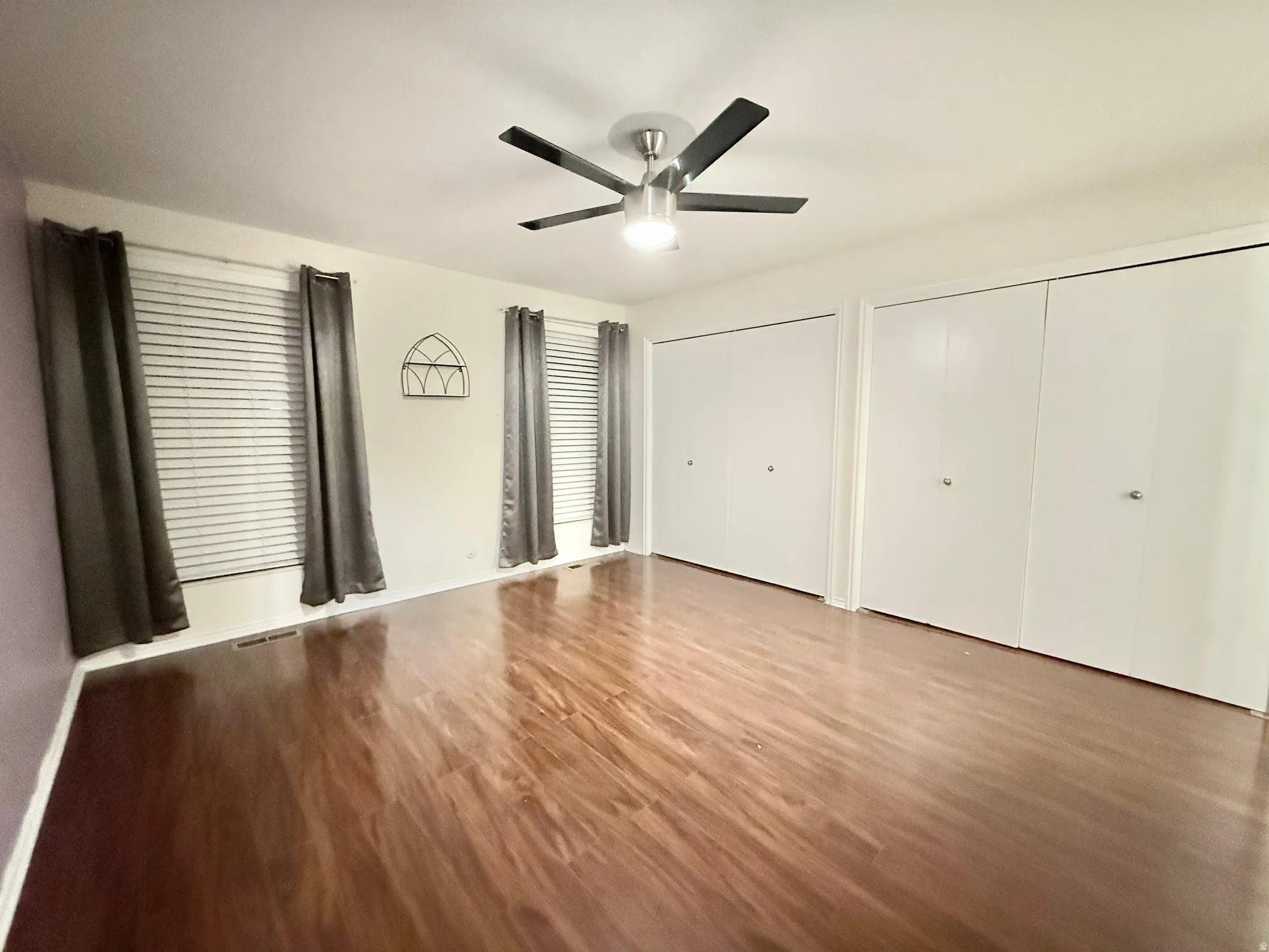 Unfurnished bedroom with multiple closets, wood finished floors, and a ceiling fan