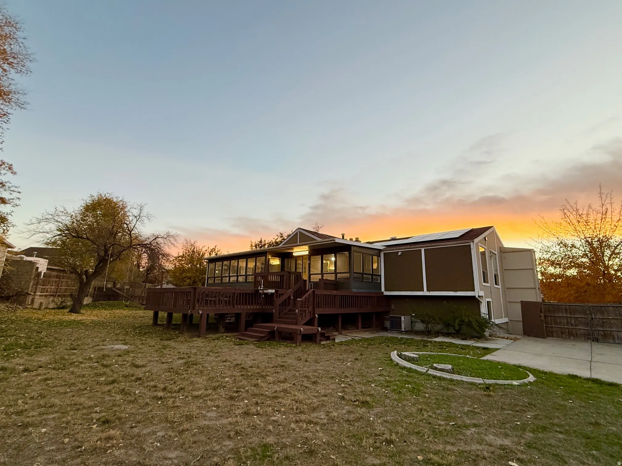 Back of property at dusk with a wooden deck, a sunroom, roof mounted solar panels, and stairway