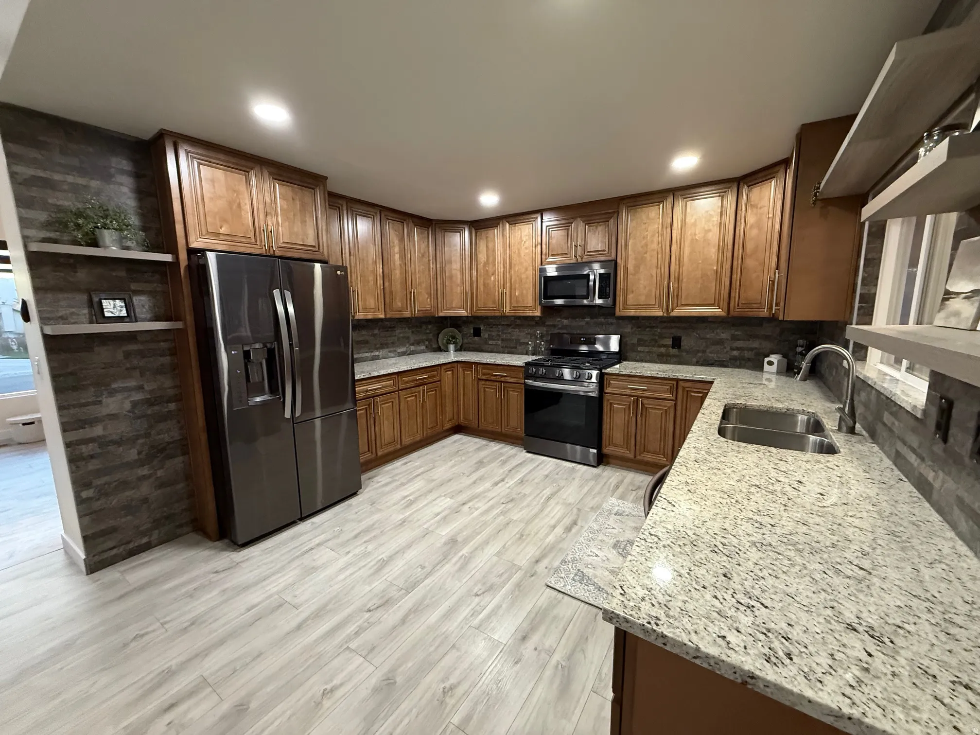 Kitchen featuring light stone counters, stainless steel appliances, tasteful backsplash, open shelves, and brown cabinets