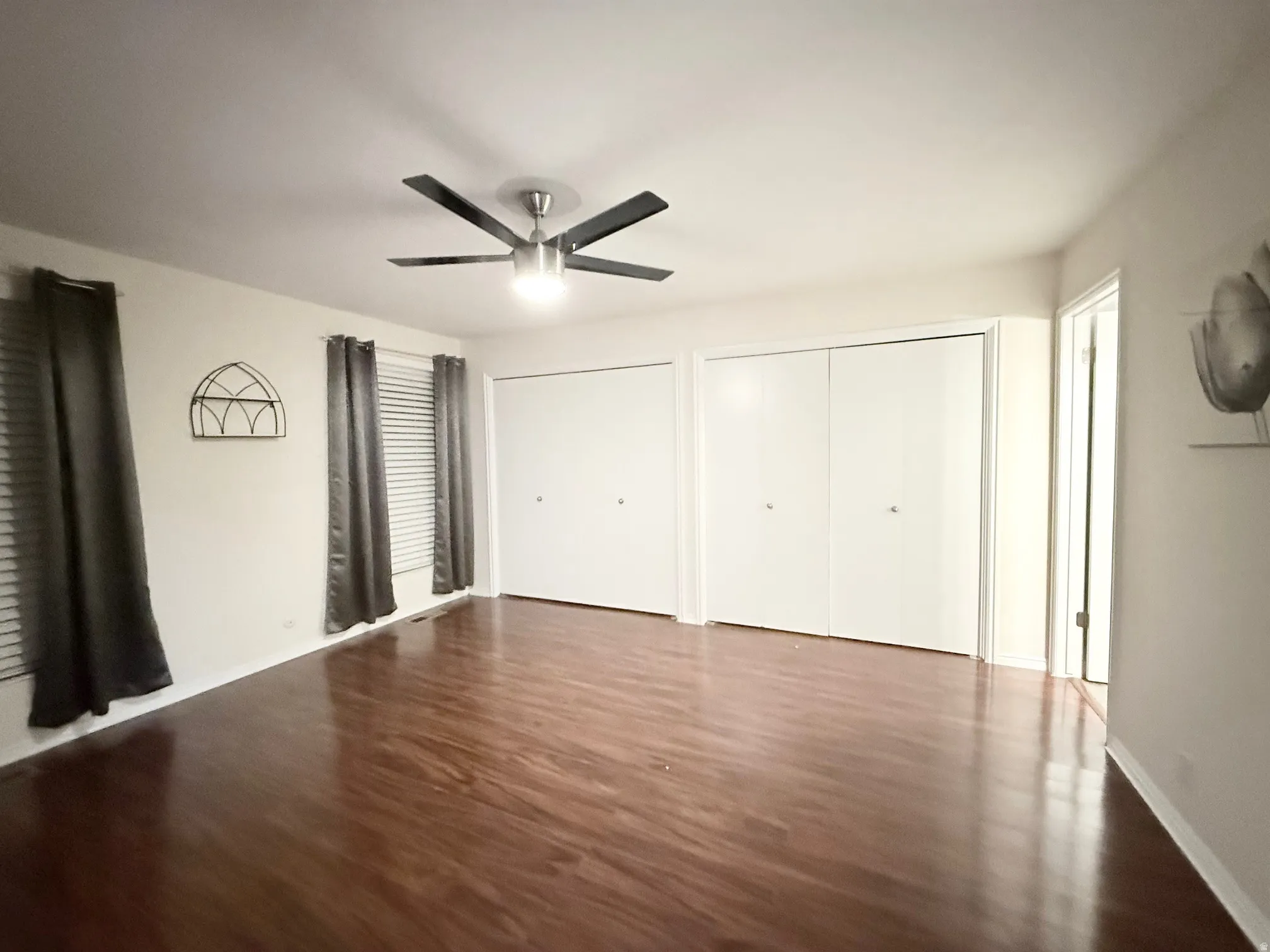 Unfurnished bedroom featuring multiple closets, dark wood-style floors, and ceiling fan