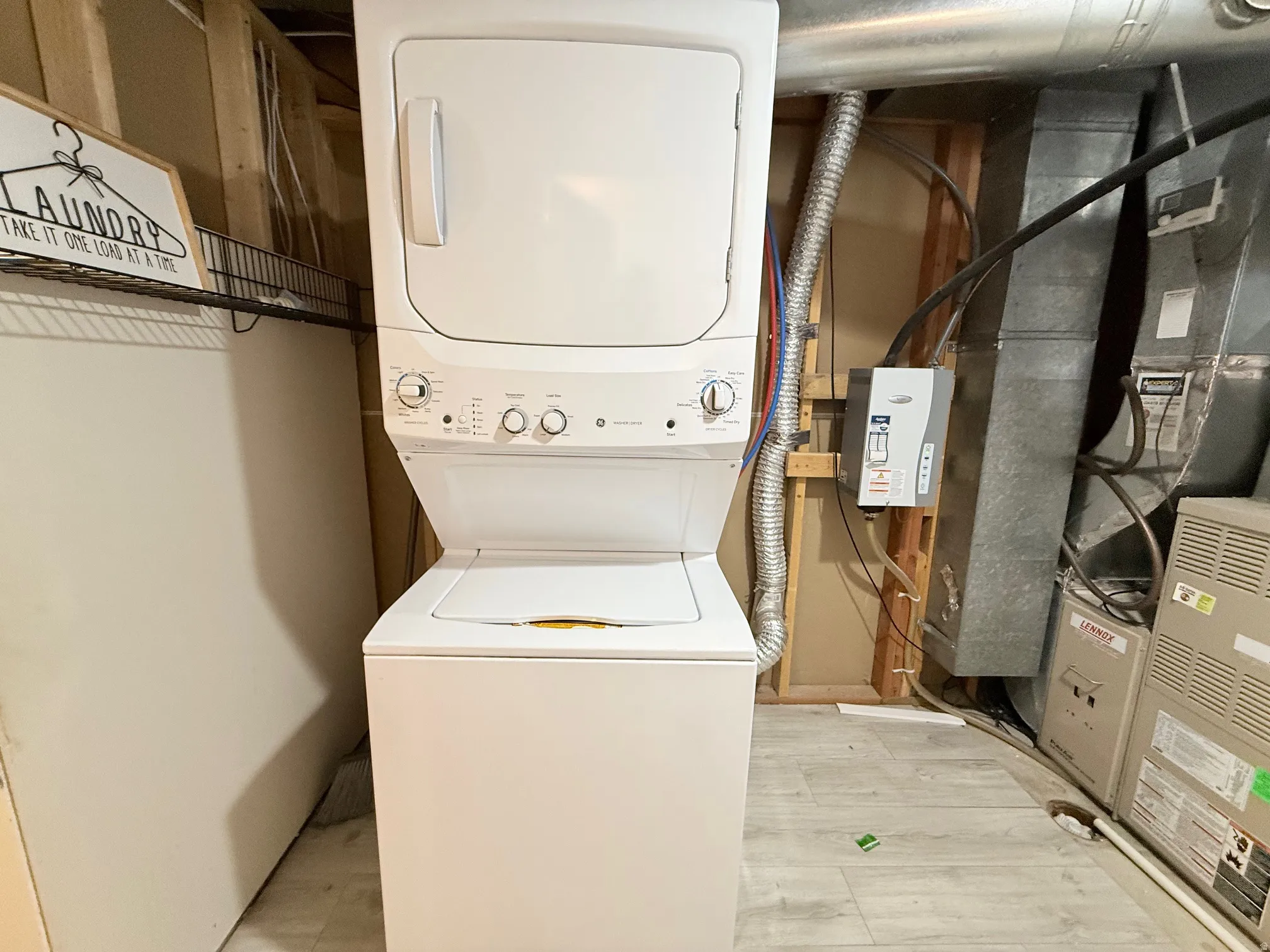 Laundry area with heating unit, stacked washer / drying machine, and light wood-style flooring