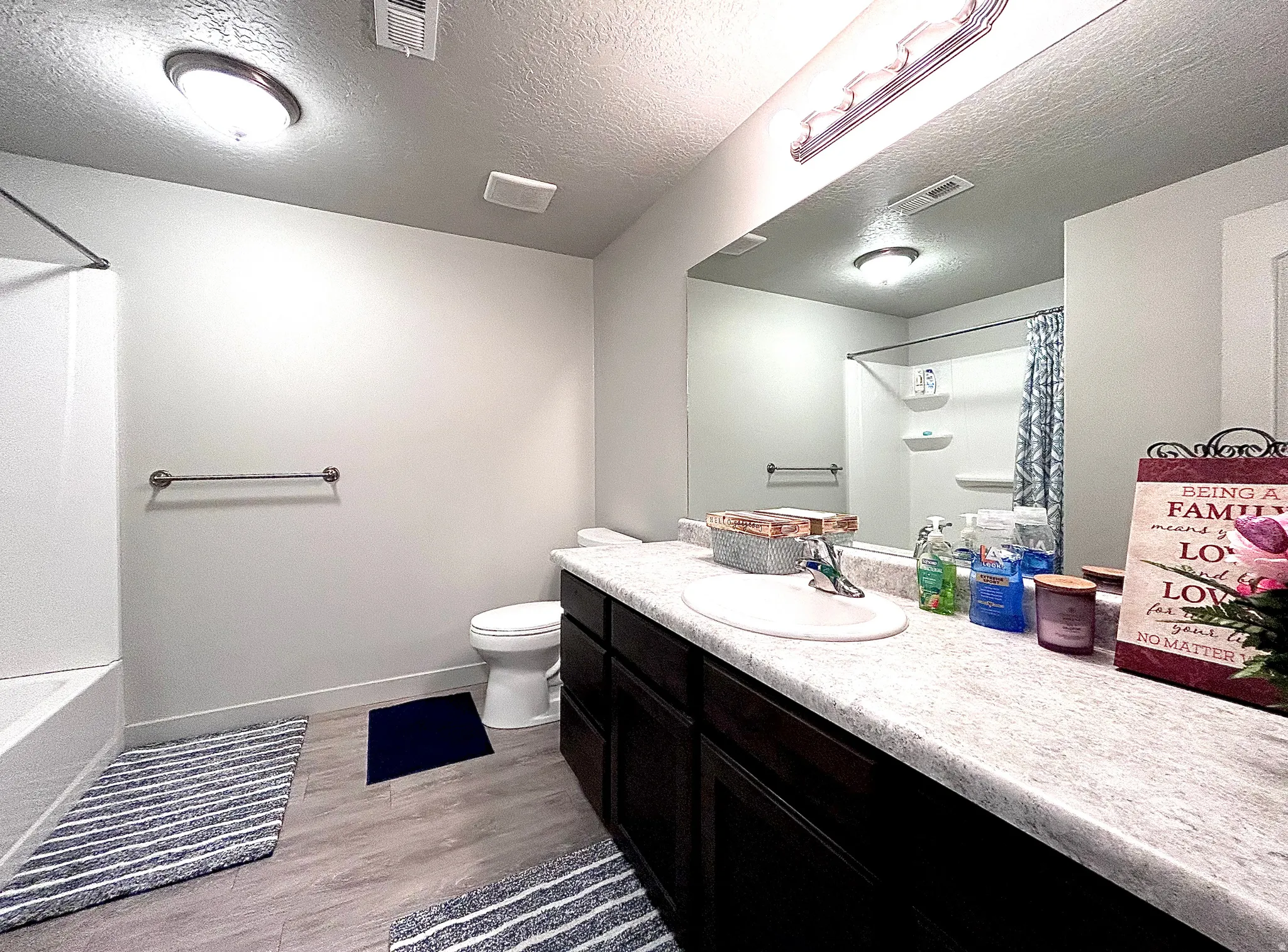 Full bath with a textured ceiling, light wood-style floors, vanity, and shower / bath combo with shower curtain
