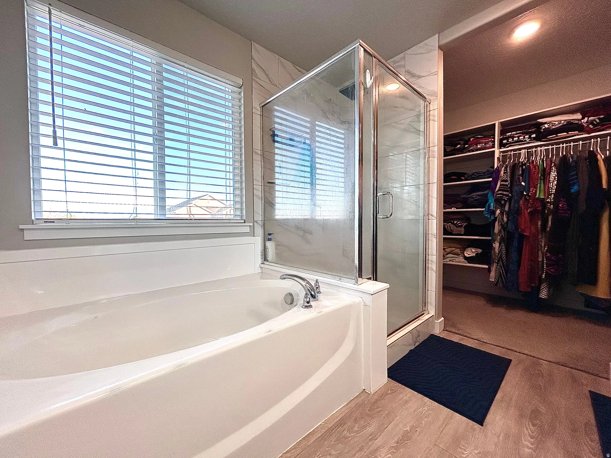 Full bathroom featuring a spacious closet, a bath, light wood-style floors, and a shower stall